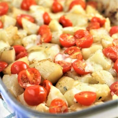 roast potatoes with mozzarella and cherry tomatoes in a blue baking dish