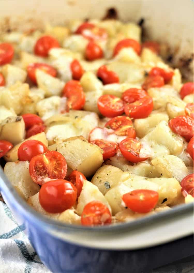 roast potatoes with mozzarella and cherry tomatoes in a blue baking dish