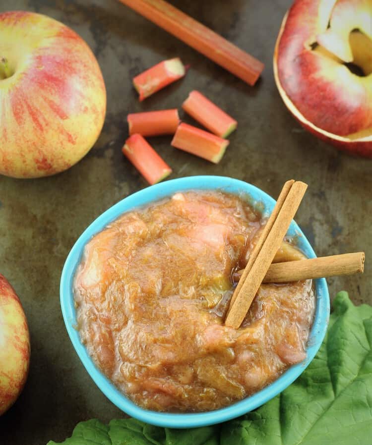 rhubarb applesauce in a blue bowl surrounded by apples and rhubarb