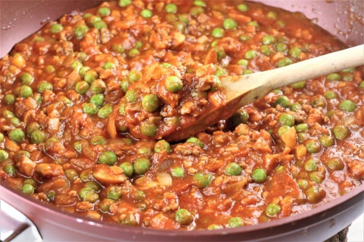 pan full of meat sauce with peas being scooped into a wooden spoon