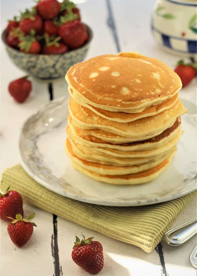 stack of pancakes with bowl of strawberries in background