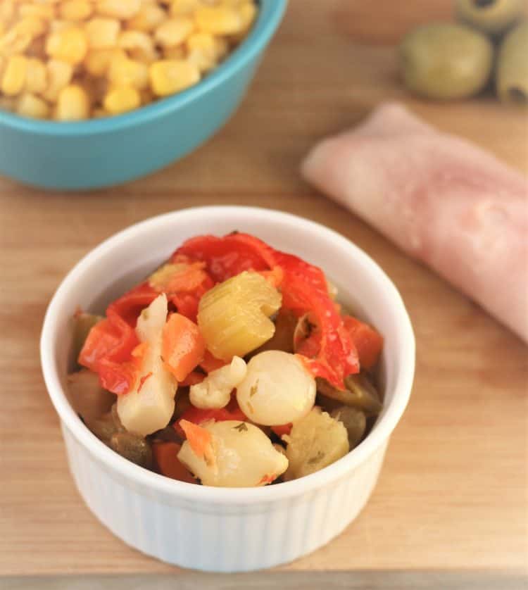 bowl of mixed Italian giardiniera with corn, olives and ham in background
