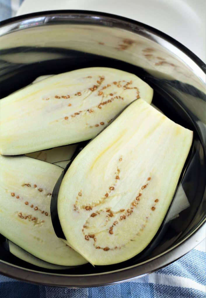 sliced eggplants submerged in a bowl of water