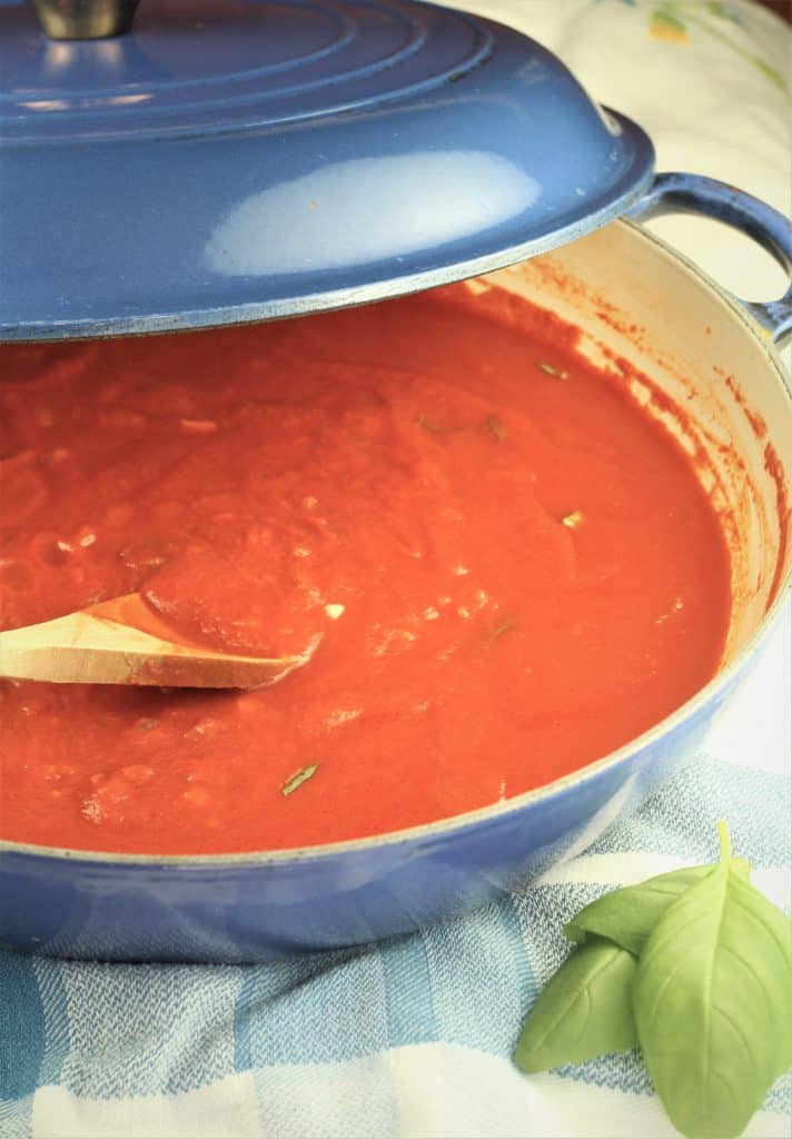 pot filled with tomato sauce with spoon resting in it, basil leaves on side
