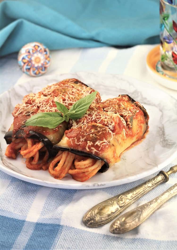 2 eggplant involtini with maccaruna on a white plate with utensils on side