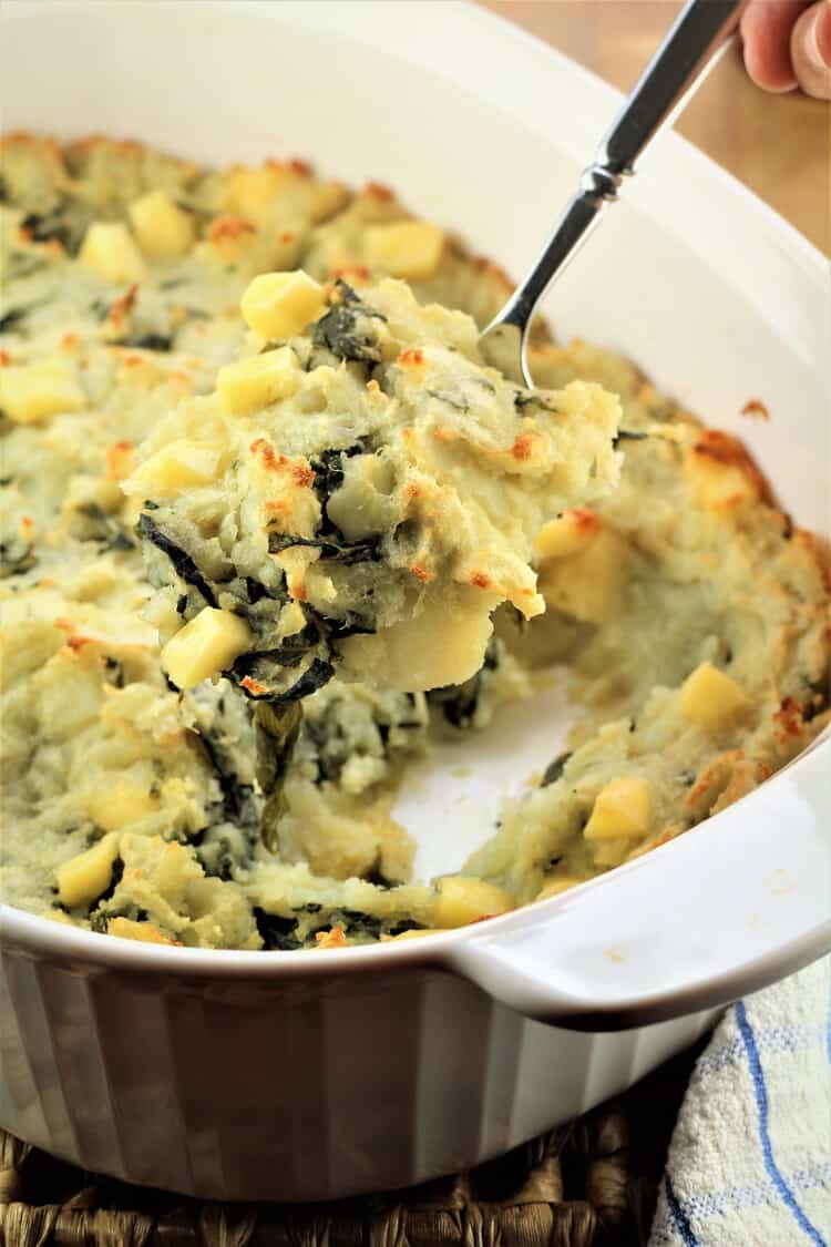 spoonful of cheesy swiss chard and potato casserole being lifted from baking dish