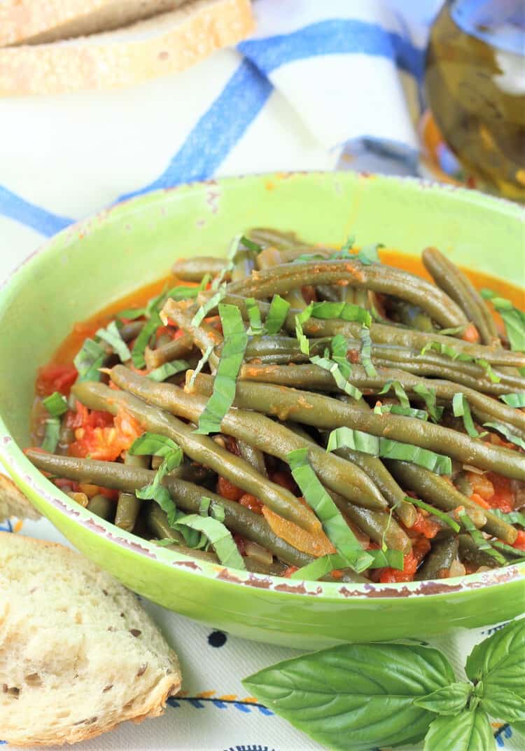bowl of stewed green beans with tomatoes with chunk of bread and fresh basil 