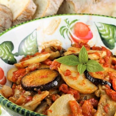 Eggplant and potato slices with tomato sauce in bowl.