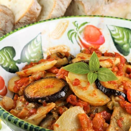 Eggplant and potato slices with tomato sauce in bowl.