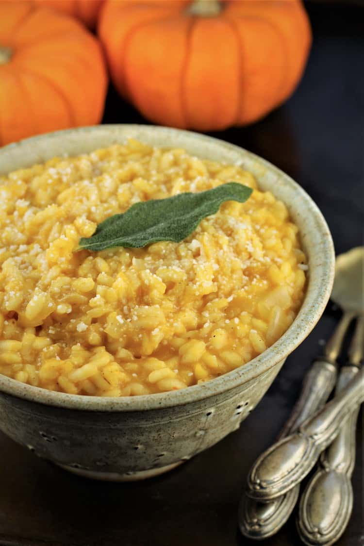 bowl of pumpkin risotto with spoons on the side and pumpkins behind it