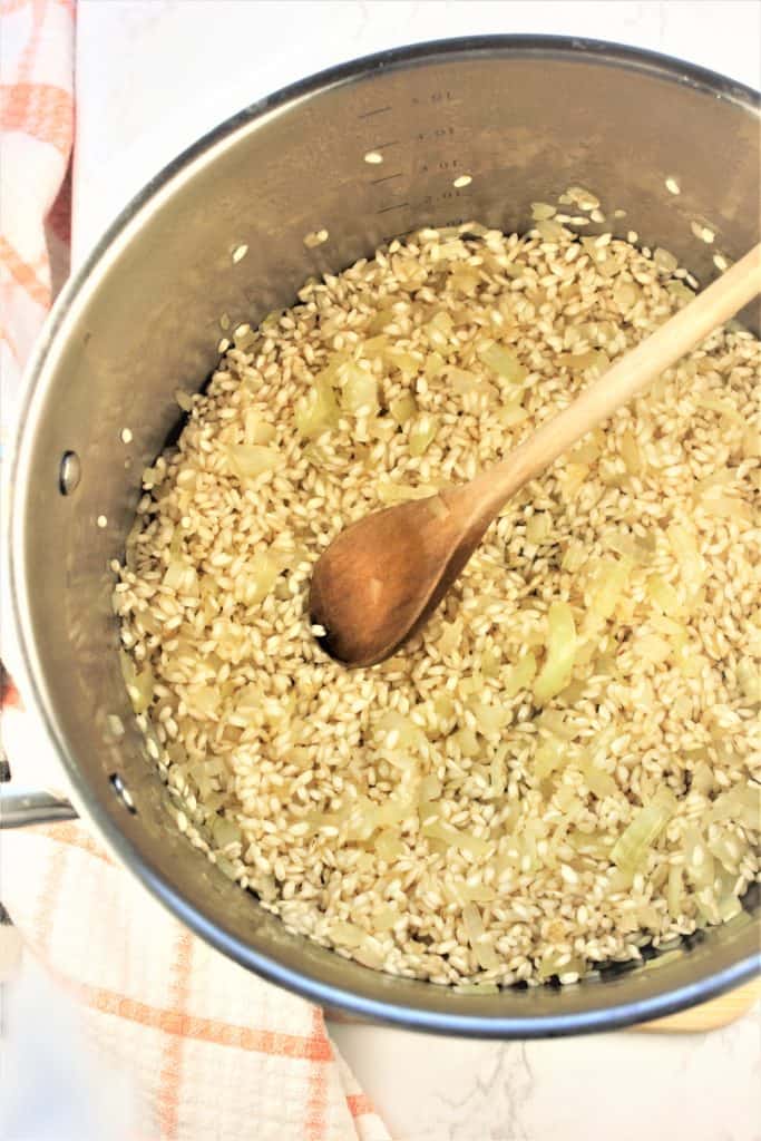 saucepan with sauteed rice and onions with wooden spoon