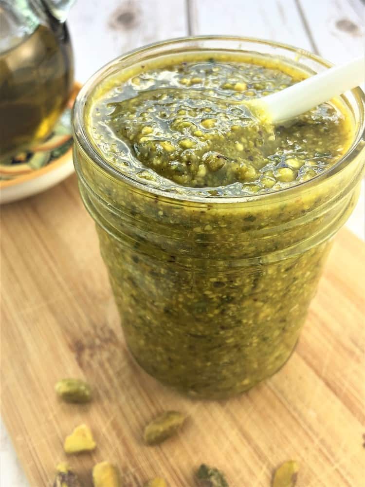 glass jar filled with pistachio pesto with spoon in it 
