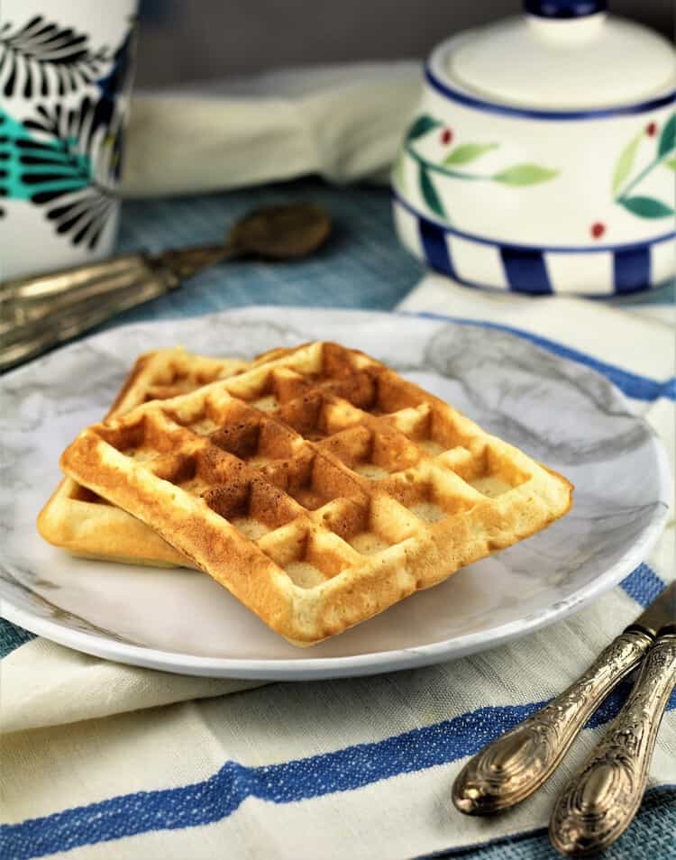 plate with 2 waffles next to cutlery and sugar bowl 