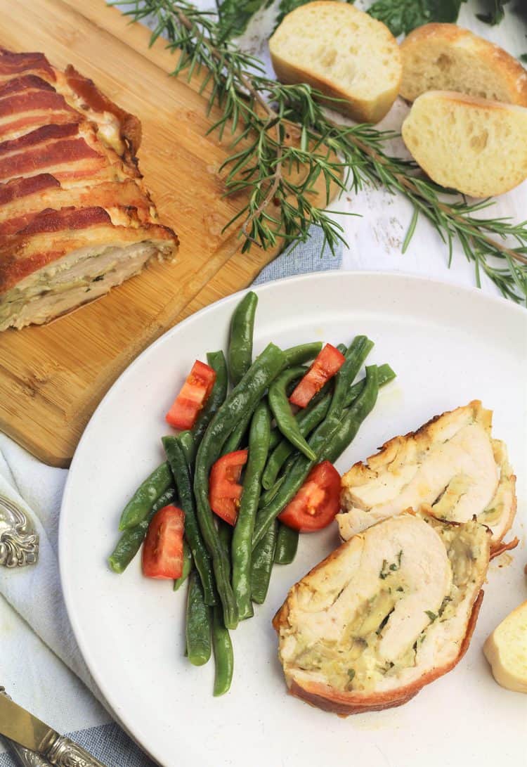 sliced stuffed turkey roulade on plate with green bean salad next to wood board with roast turkey