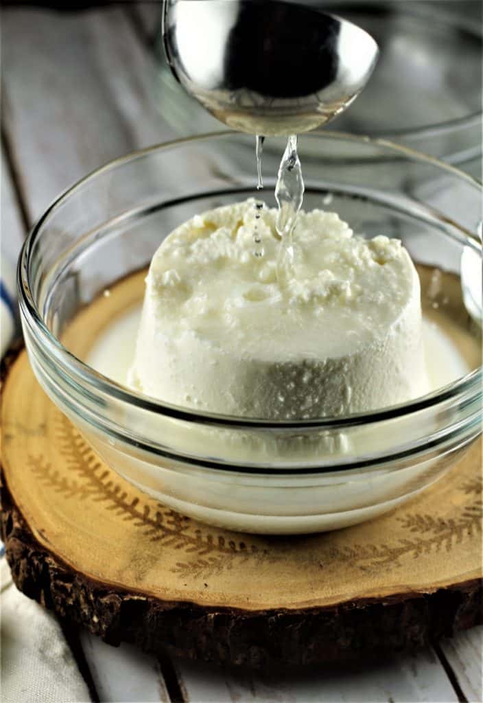 Ricotta in a glass bowl with pasta water being ladled over it.