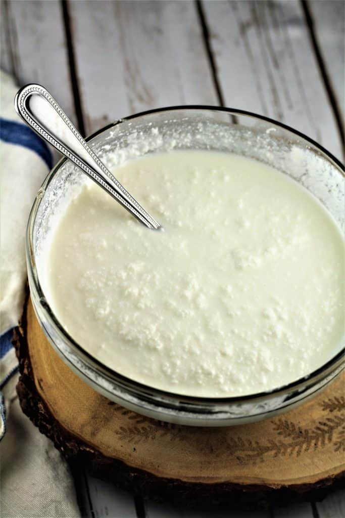 Creamy ricotta sauce in a glass bowl with spoon in it.