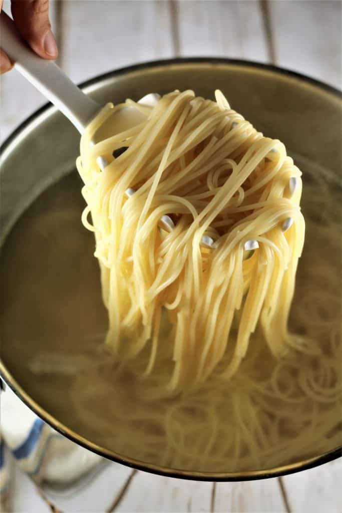 scooping spaghetti out of a pot with spaghetti scooper