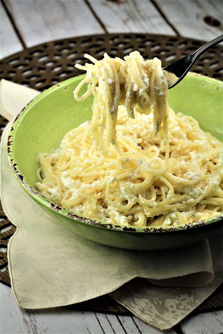 forkful of spaghetti with ricotta in a green bowl