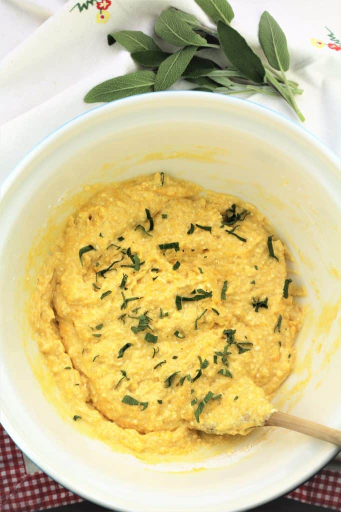 bowl with batter for savory pumpkin ricotta fritters and sage leaves behind it