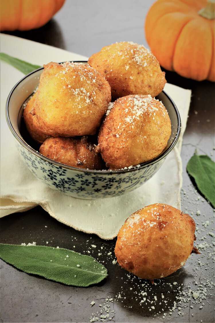 bowl of pumpkin ricotta fritters with pumpkins in background and sage leaves