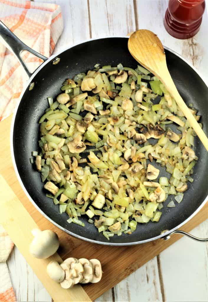 skillet with sautéed onion and mushrooms with wooden spoon , sliced mushrooms and pepper mill behind it