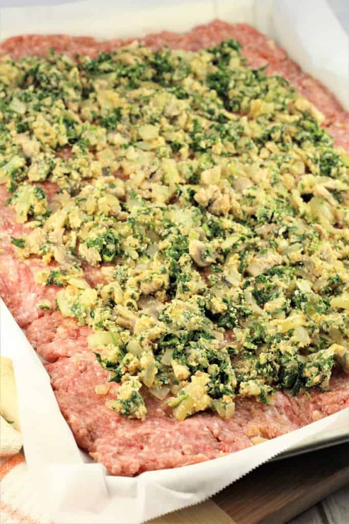 flattened ground meat on sheet pan covered with spinach mushroom mixture