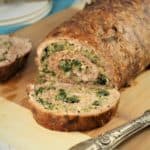 Sliced spinach and mushroom filled pinwheel meatloaf on a cutting board with utensils