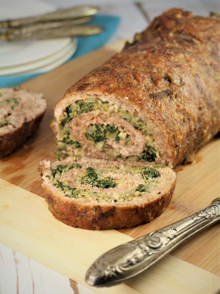 spinach and mushroom filled rolled meatloaf sliced on a cutting board