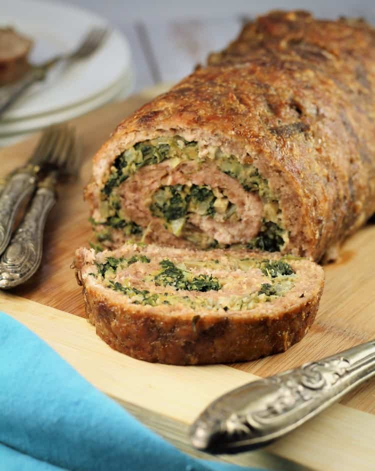 sliced Spinach and Mushroom Filled Pinwheel Meatloaf on wooden board with utensils