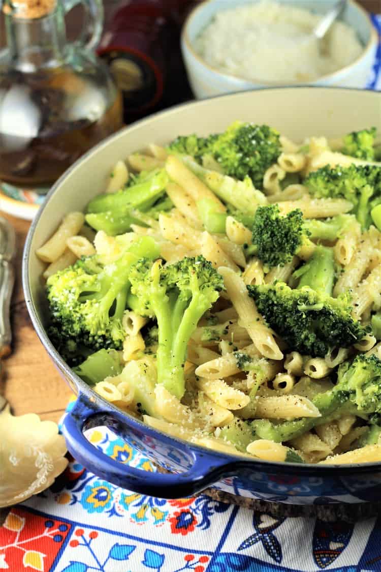 blue pan filled with pasta and broccoli with olive oil bottle and bowl of cheese in background