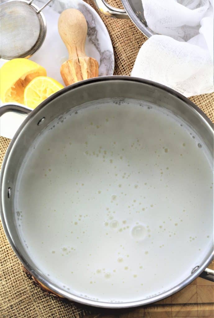 pot of boiling milk with halved juiced lemon and juicer behind it
