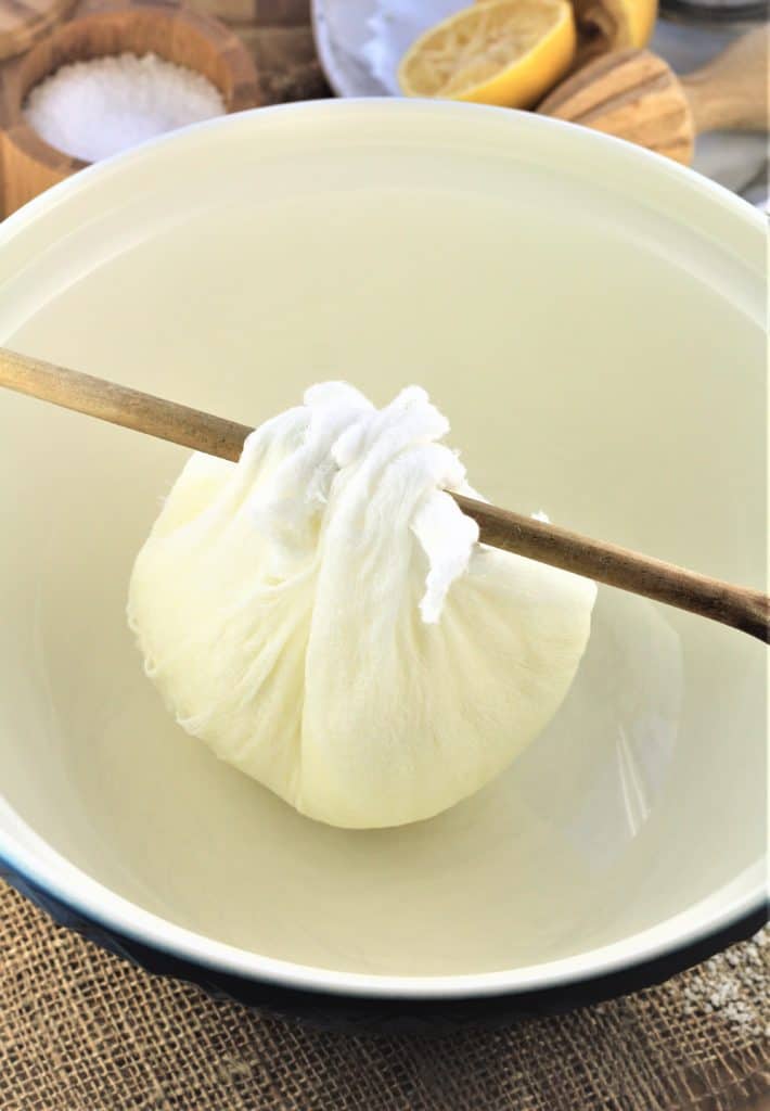 bundle of ricotta tied in cheesecloth draining over bowl