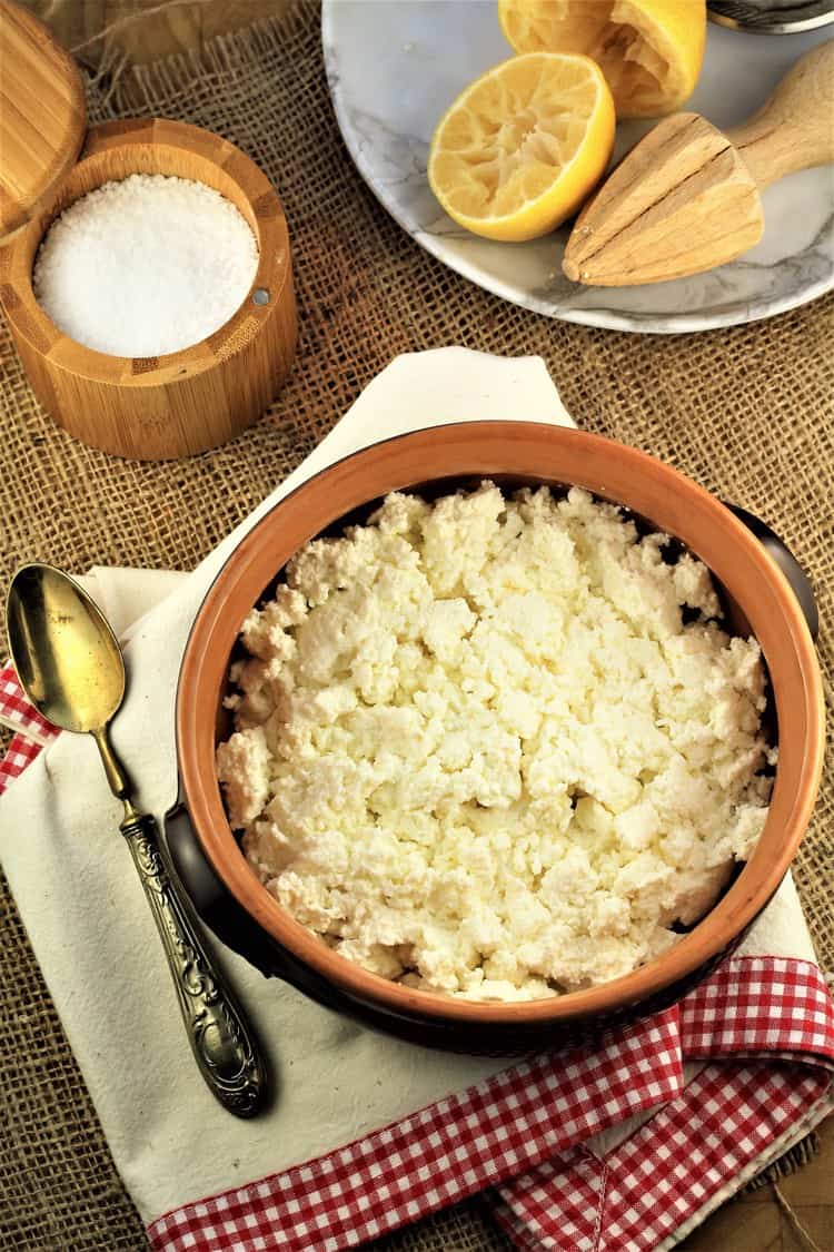 bowl of fresh ricotta curds on dish towel with spoon, halved lemon and container of salt