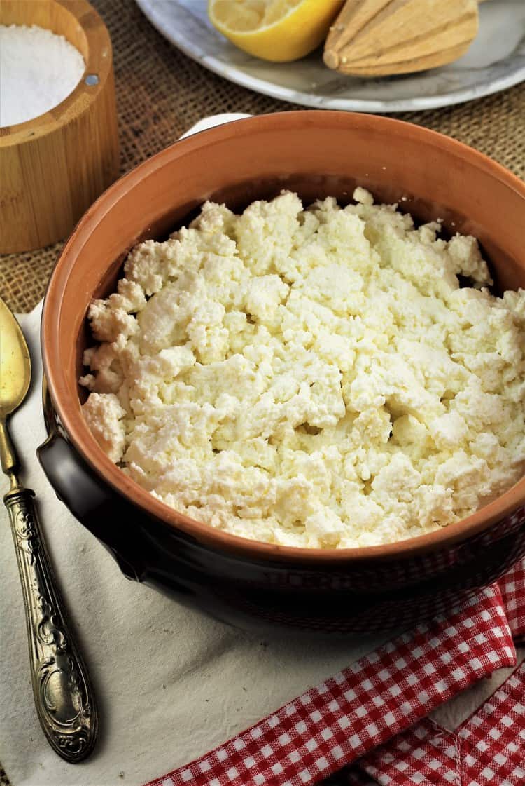 bowl filled with fresh ricotta curds on dish towel with spoon, halved juiced lemon and salt