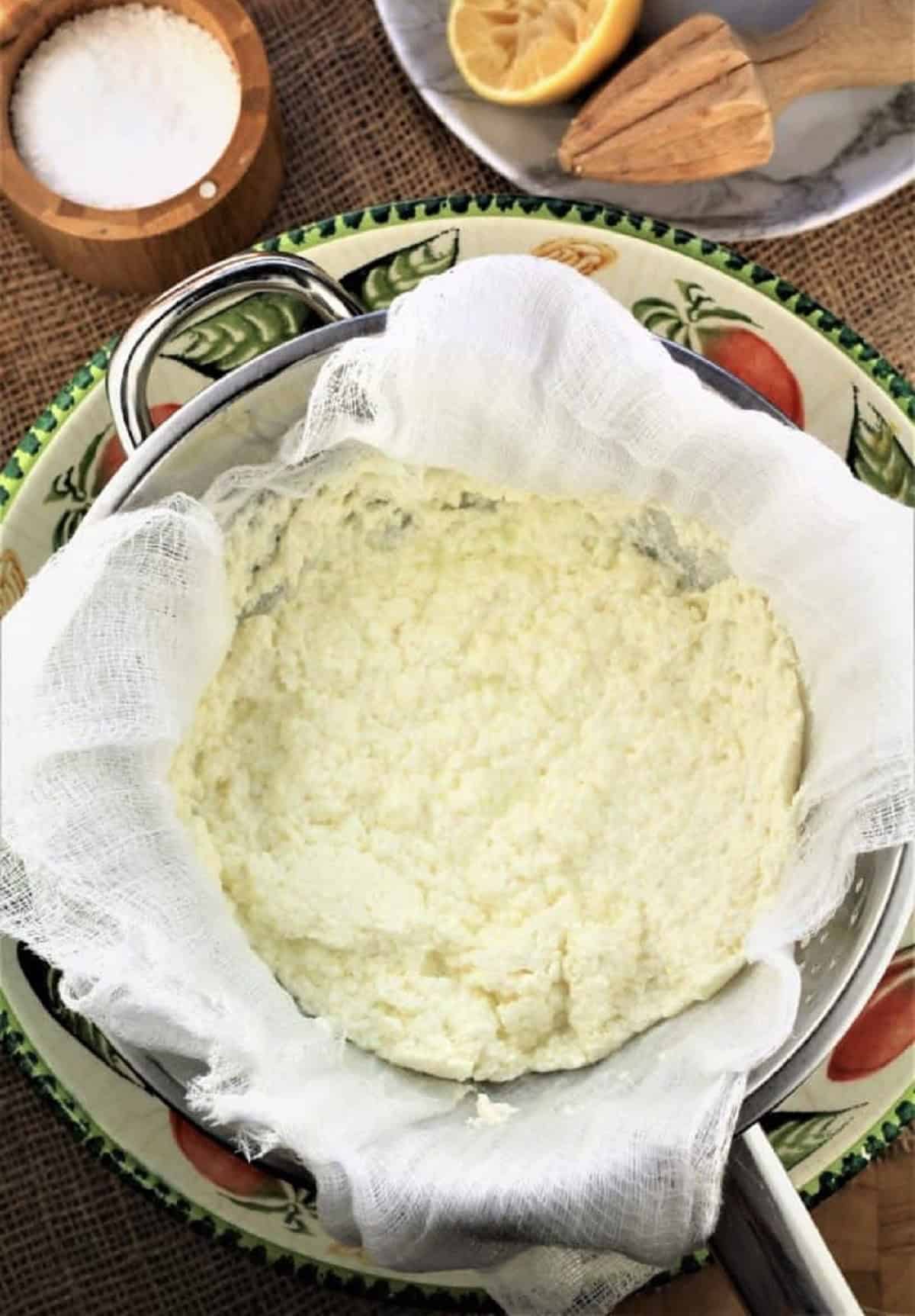 Homemade ricotta draining in cheese cloth lined sieve over bowl.