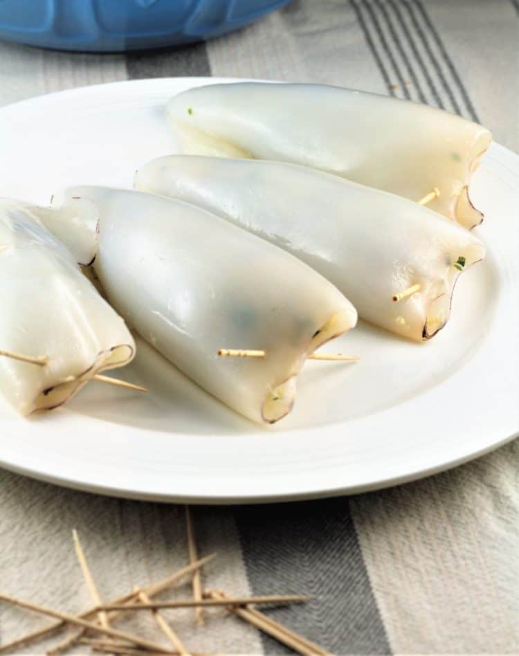 stuffed calamari tubes on white plate with toothpicks to secure the ends