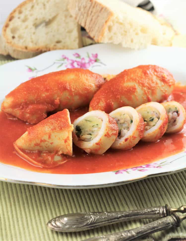 plate with sliced stuffed calamari on tomato sauce with bread slices in background