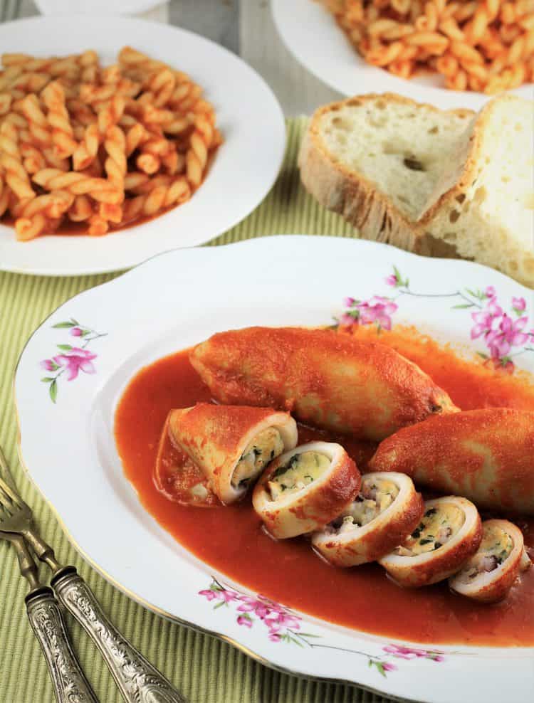 plate with stuffed calamari surrounded by plates of pasta in tomato sauce and bread slices