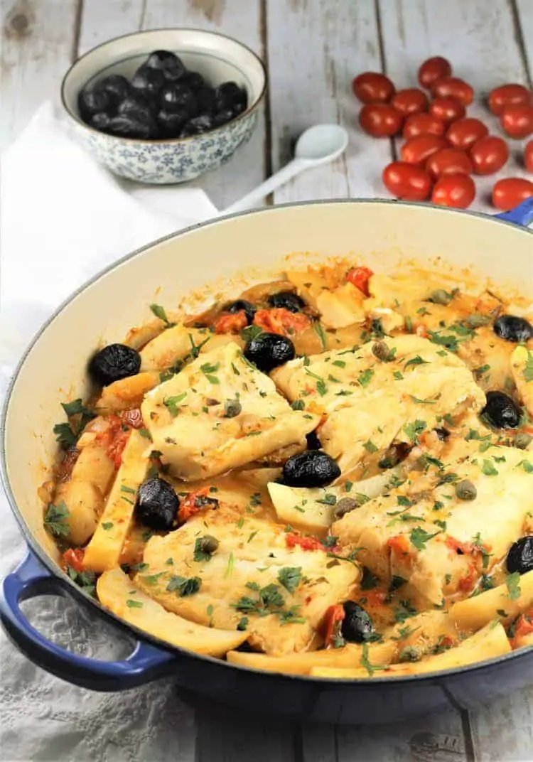 blue skillet with salt cod pieces surrounded by olives and black olives