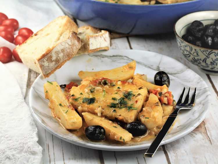 white plate with salt cod, potatoes and olives surrounded by sliced bread