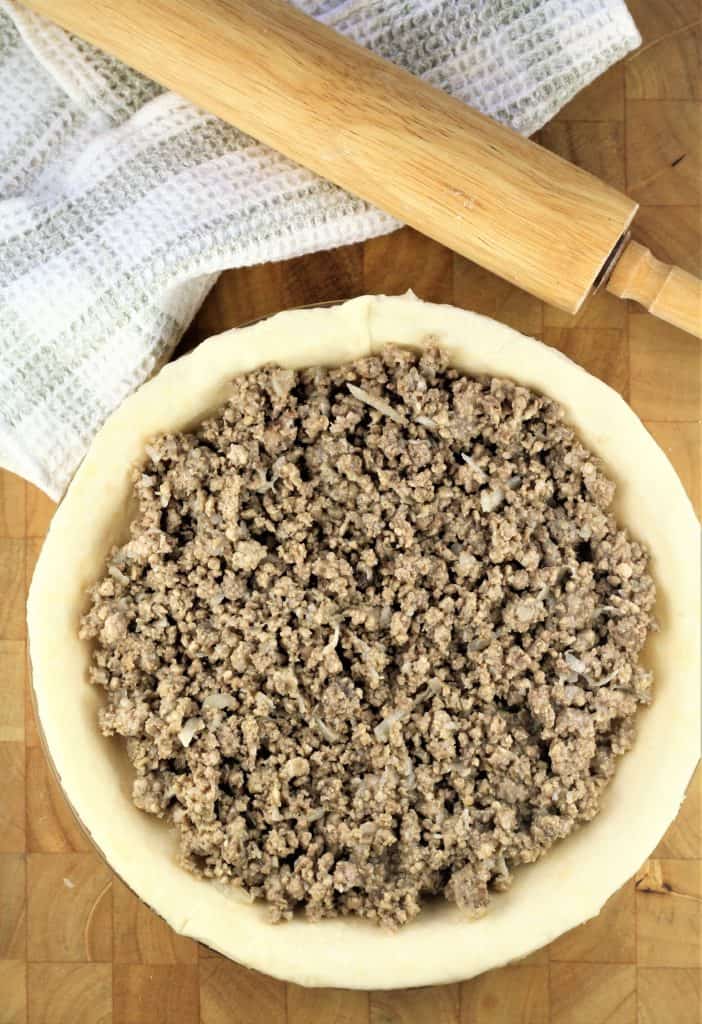 pie crust filled with meat filling and rolling pin behind it