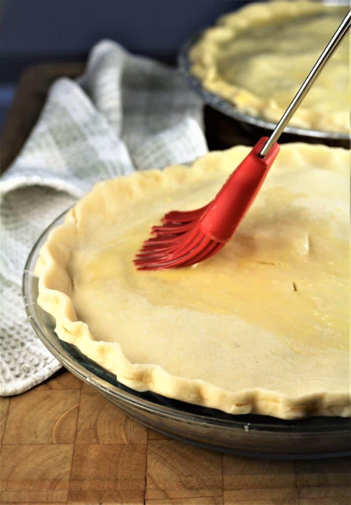 raw pie crust being brushed with egg wash