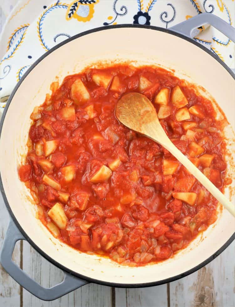 large skillet with tomato sauce, potatoes and wooden spoon