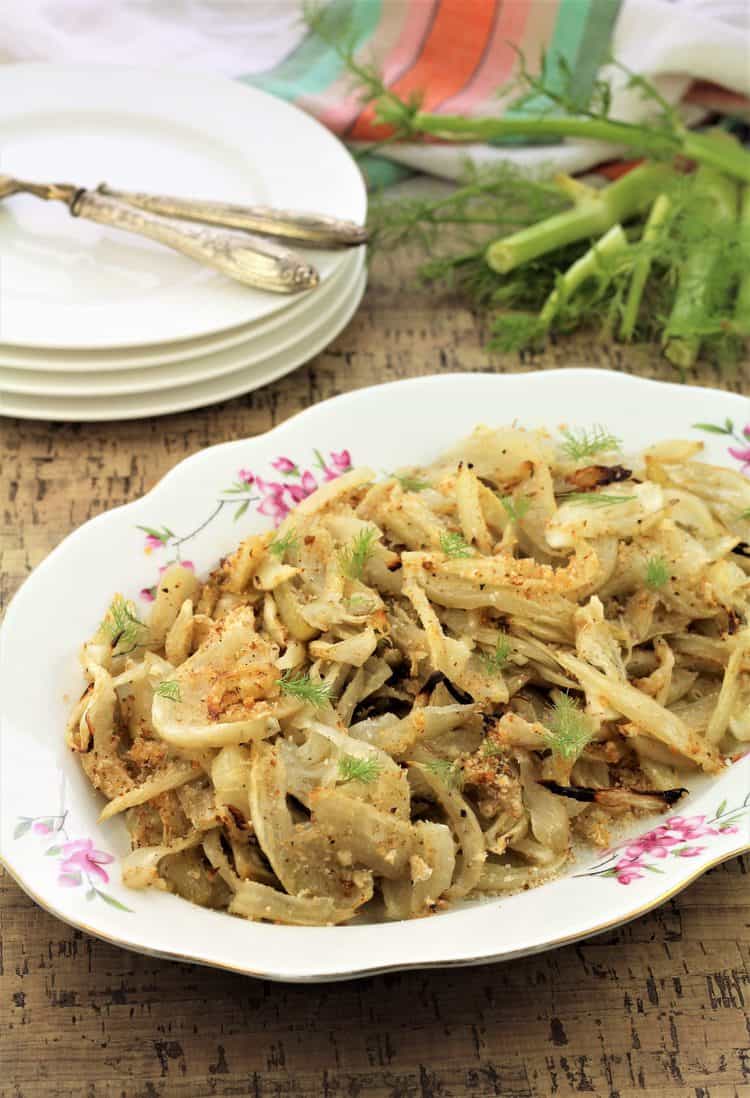 roasted fennel on oval plate with fennel stalks and stack of plates in background