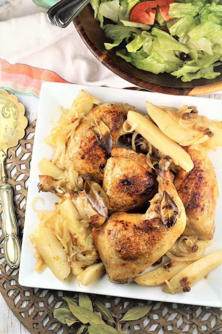 white square plate with roast chicken and potatoes with salad in background