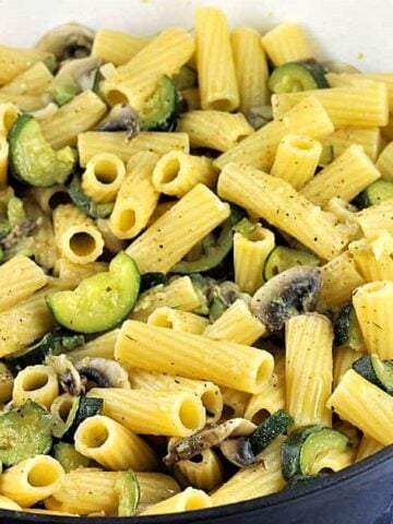 Pasta with zucchini and mushrooms in skillet.
