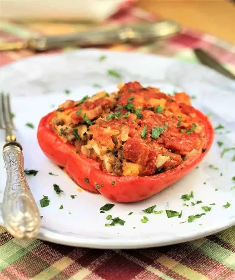 stuffed red pepper half on white plate sprinkled with parsley and fork on side