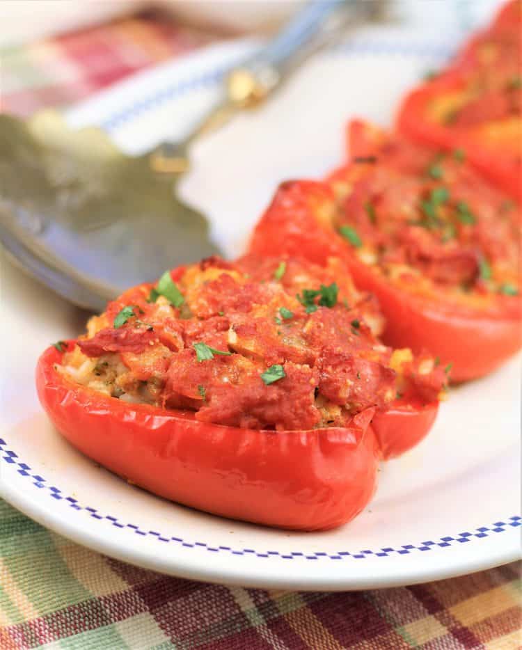 white plate with 3 stuffed red peppers with meat and rice and serving spoon