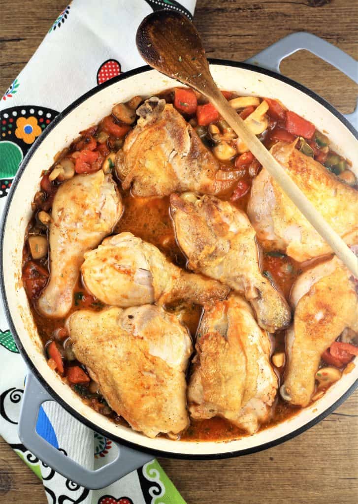 chicken pieces cooking in tomato sauce in large skillet with wooden spoon on side