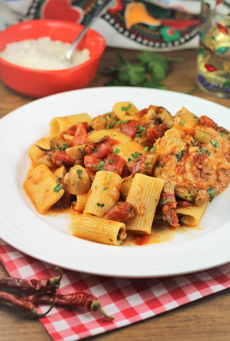 plate of pasta with tomato sauce and chicken cacciatore with bowl of cheese in background and red chili peppers in foreground